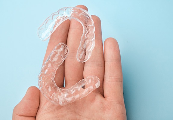 Bird’s eye view of two clear aligners on the palm of a hand with light blue background