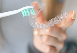 Someone brushing clear aligners with white toothbrush with green bristles