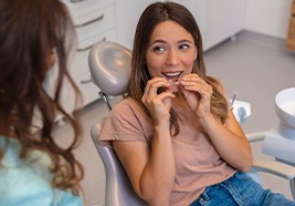 Woman in tan shirt in dental chair inserting clear aligners