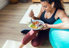Woman in exercise clothing sitting on her floor and eating a salad
