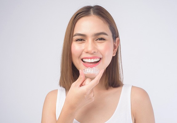 patient smiling while holding SureSmile clear aligner in Lewisville?