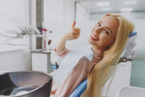 Smiling woman in dentist chair giving a thumbs-up